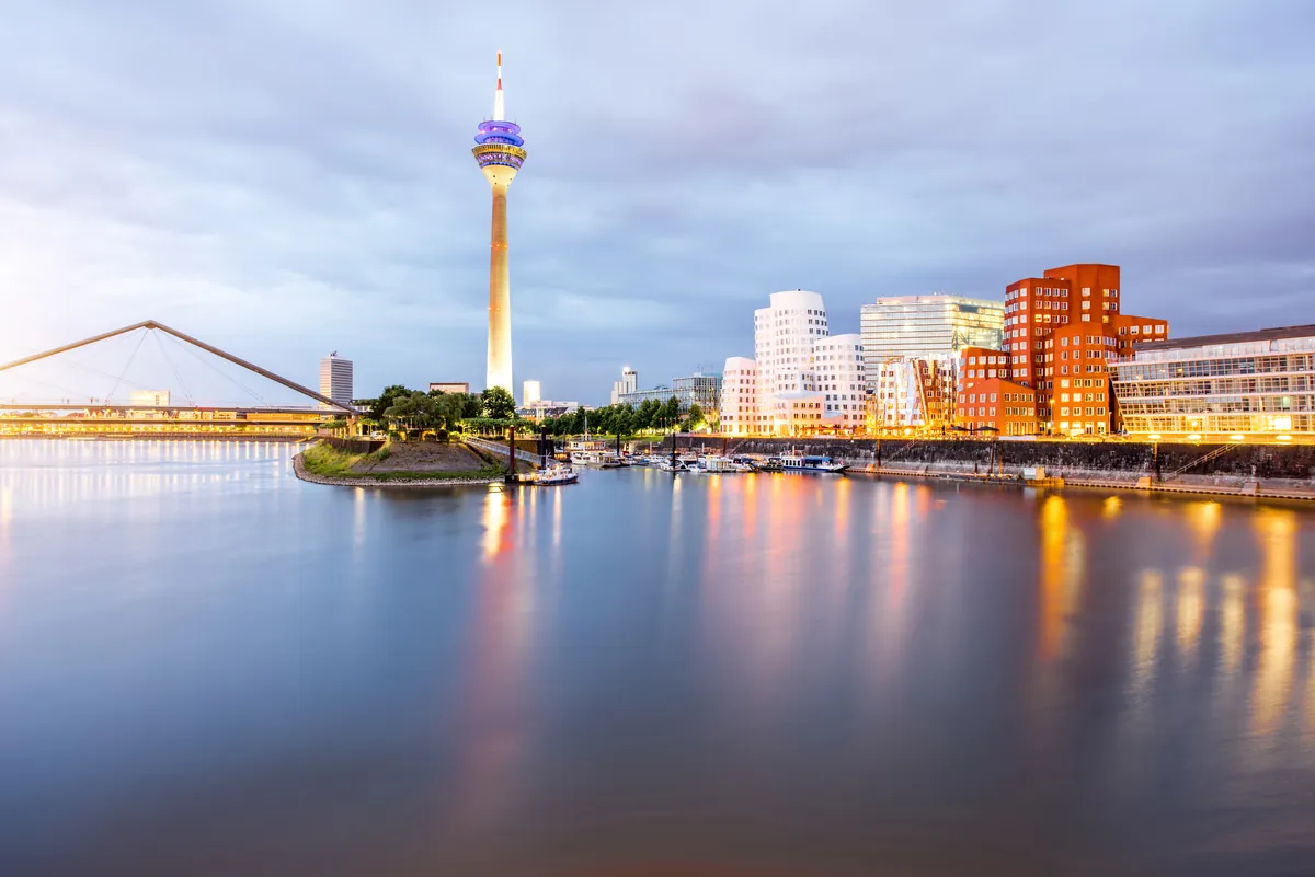 Der Rheinturm und die geschwungenen Gehry-Bauten im Düsseldorfer MedienHafen, in der Dämmerung im ruhigen Wasser gespiegelt