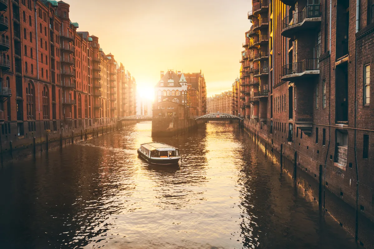 Ein Kanal zwischen hohen Backsteinspeichern in Hamburg zur goldenen Stunde, ein kleines Boot auf dem Wasser