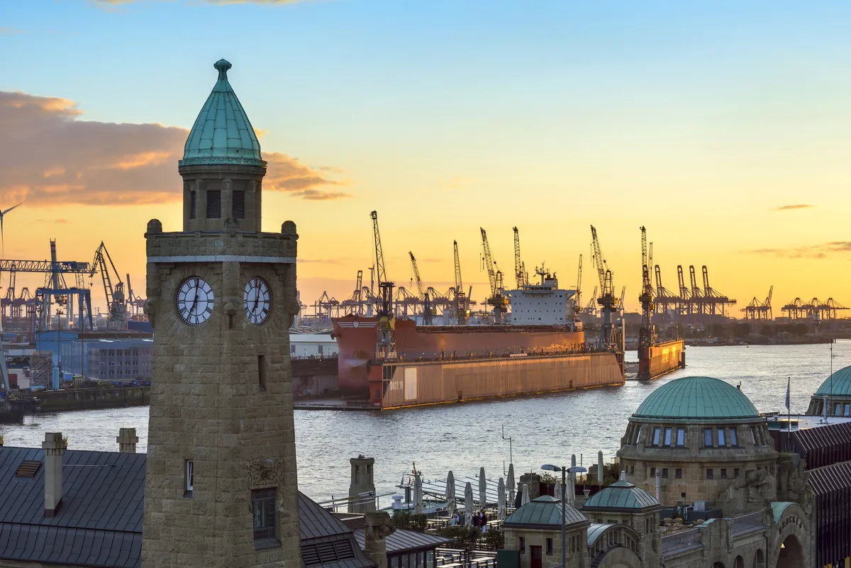 Der Uhrturm der St. Pauli Landungsbrücken in Hamburg bei Sonnenuntergang, dahinter Hafenkräne