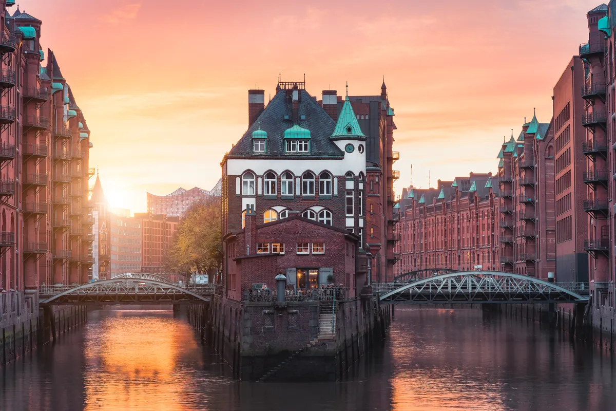 Die Backsteinlagerhäuser und Brücken der Hamburger Speicherstadt spiegeln sich bei Sonnenuntergang im Kanal