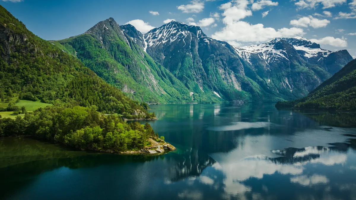 Der stille Eikesdalsvatnet in Norwegen spiegelt steile grüne Berge und schneebedeckte Gipfel