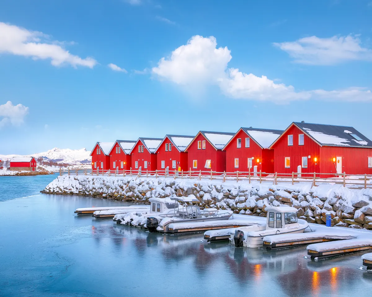 Eine Reihe roter hölzerner Fischerhütten am Wasser an einer verschneiten Nordküste