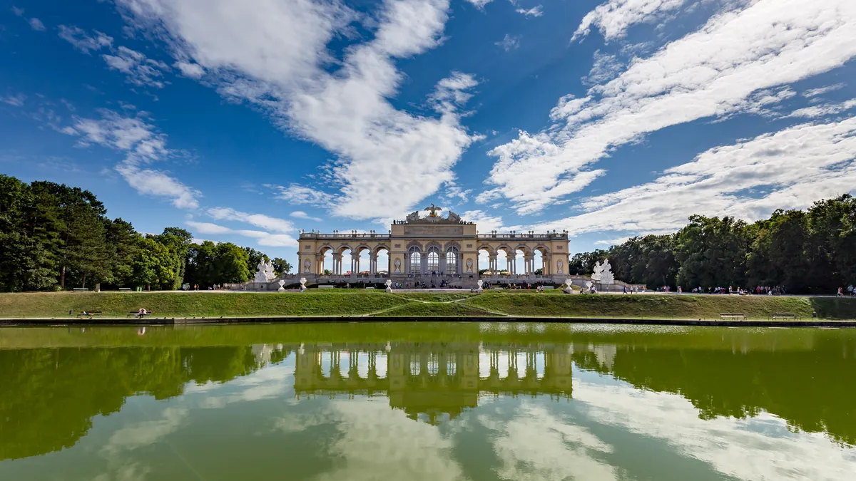 Die Gloriette über den Gärten von Schloss Schönbrunn in Wien, im Teich gespiegelt unter blauem Himmel